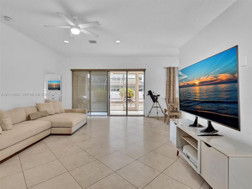 Open-concept interior featuring large-format diagonal tile flooring, high ceilings with a centralized lighted ceiling fan, and sliding glass doors with screen enclosure