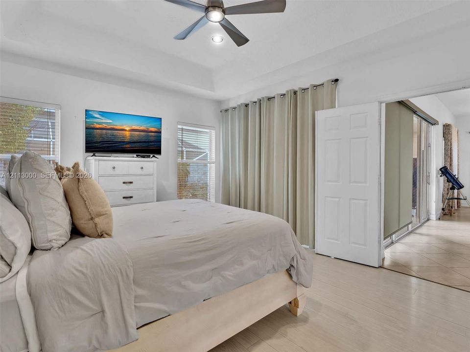 Tray ceiling with a central multi-blade ceiling fan, neutral wall finishes, tile flooring, and dual-panel interior doors