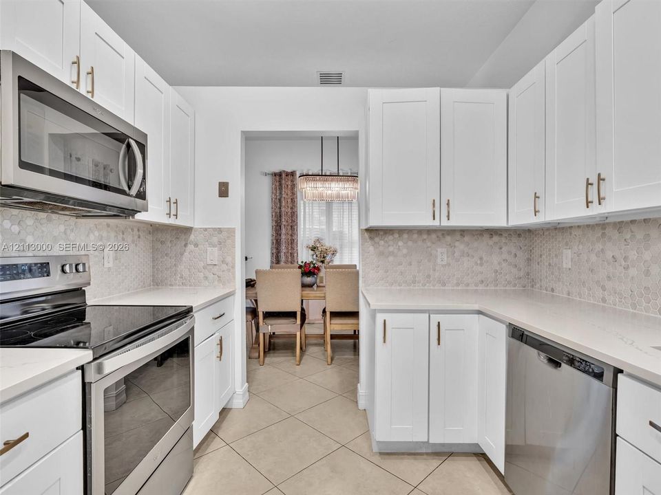 Kitchen featuring white shaker-style cabinetry, stainless steel appliances, neutral stone-finish countertops, and a hexagonal tile backsplash