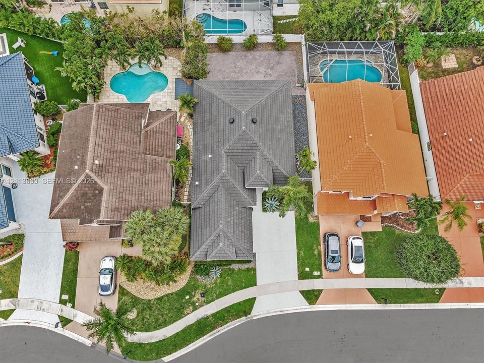 Aerial perspective featuring a multi-pitched tile roof, concrete driveway, stone-paved walkway, and landscaped front yard