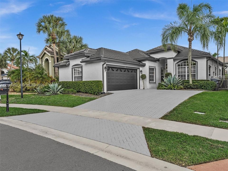 Stucco exterior with a multi-hipped tile roof, decorative arched window accents, and a paved driveway leading to a two-car garage