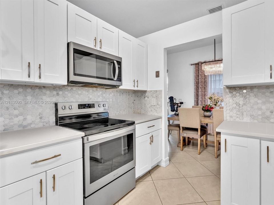 Kitchen featuring white Shaker-style cabinetry, stainless steel appliances, hexagonal tile backsplash, solid-surface countertops, and tile flooring