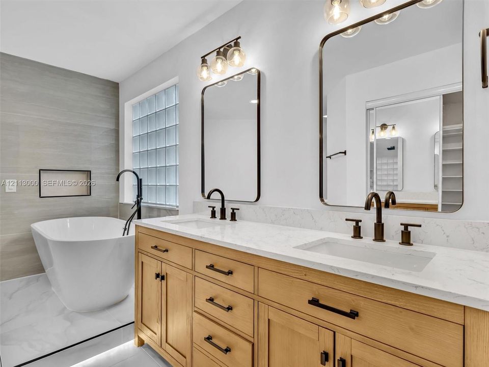 Double vanity featuring natural wood cabinetry, white stone-composite countertops, rectangular undermount sinks, and matte black fixtures