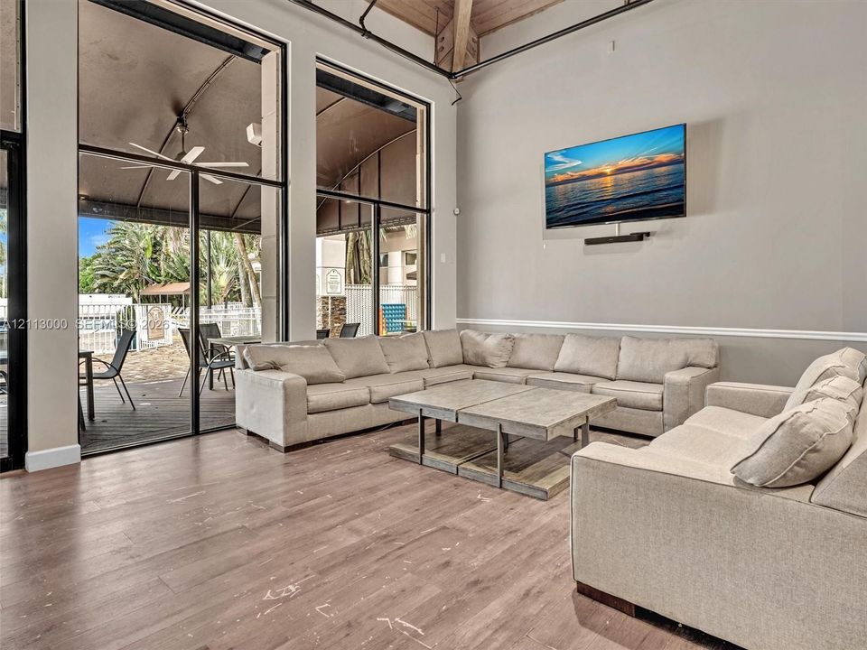 High-ceilinged common area featuring wood-finish flooring, exposed structural beams, floor-to-ceiling windows, and wall-mounted chair rail molding