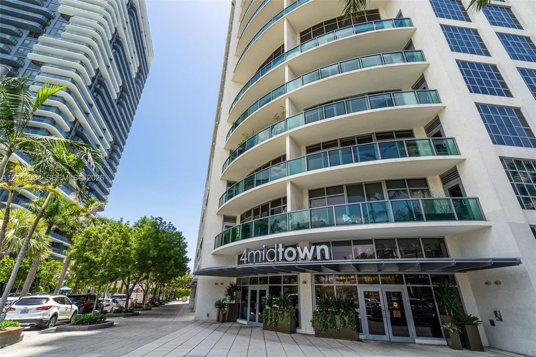 High-rise exterior featuring curved glass balconies, large window spans, white stucco façade, and ground-level storefront glass entryways
