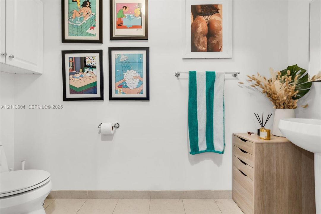 Wall-mounted white cabinetry, sleek pedestal sink, chrome hardware, and tile flooring