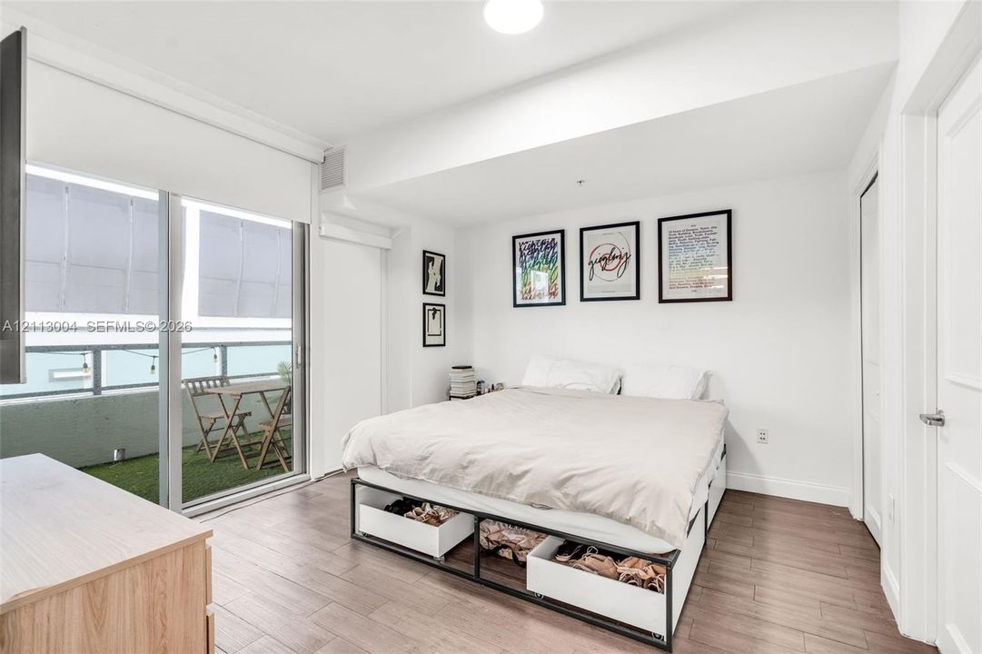 Wood-finish flooring, floor-to-ceiling sliding glass doors, and a private balcony featuring synthetic turf