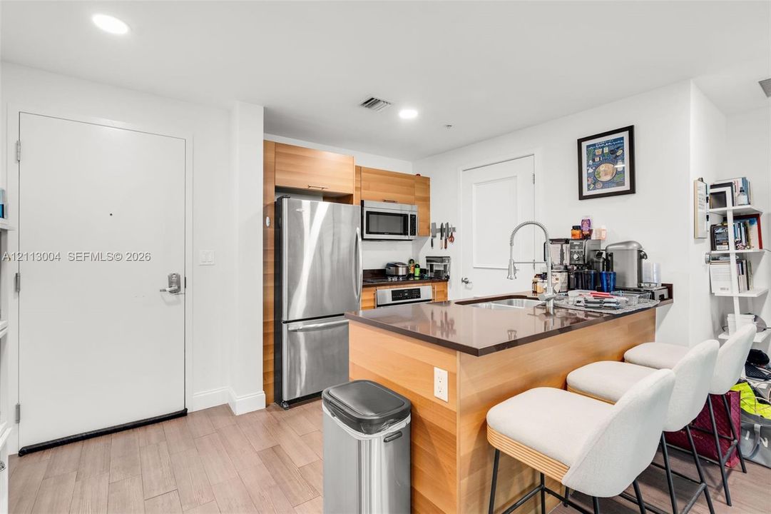 Kitchen featuring wood-finish cabinetry, dark solid-surface countertops, stainless steel appliances, a peninsula with an undermount sink, and wood-finish flooring