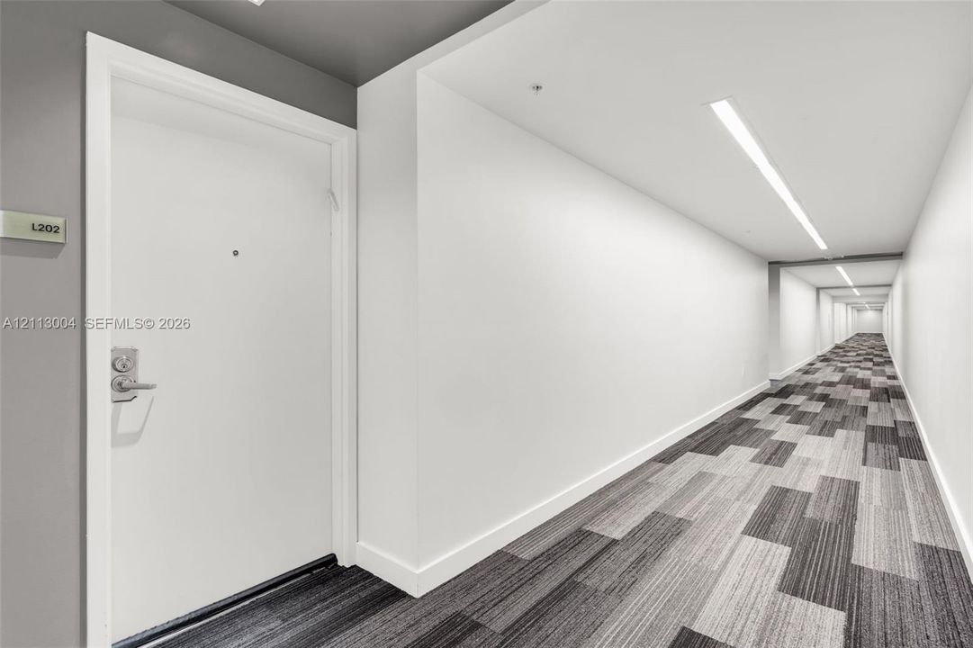 Interior corridor featuring recessed linear lighting, neutral wall finishes, and patterned modular carpeting
