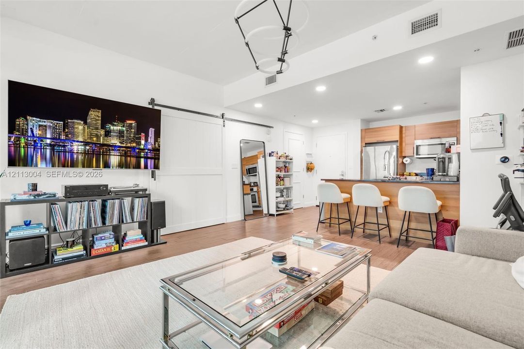Open-concept interior featuring wood-finish flooring, a kitchen breakfast bar, minimalist modern pendant lighting, and a white interior sliding barn door