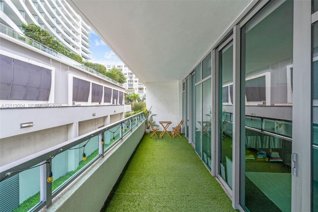 Covered balcony with synthetic turf flooring, glass railing, and floor-to-ceiling sliding glass doors