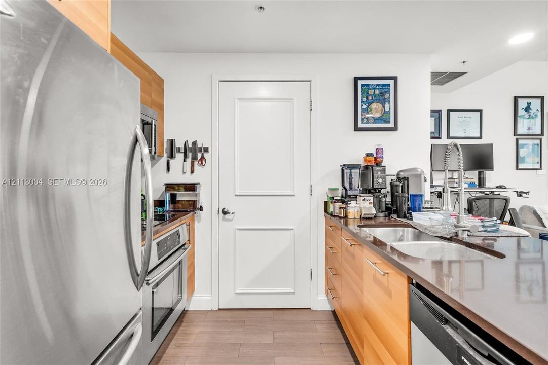 Kitchen featuring flat-panel wood-finish cabinetry, stainless steel appliances, dark composite countertops, an undermount dual-basin sink, and wood-finish flooring