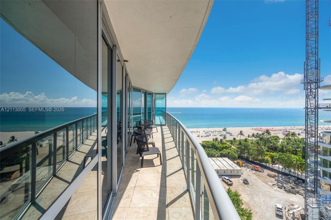 Expansive private balcony featuring stone flooring, a glass panel railing, floor-to-ceiling glass wall, and coastal scenery