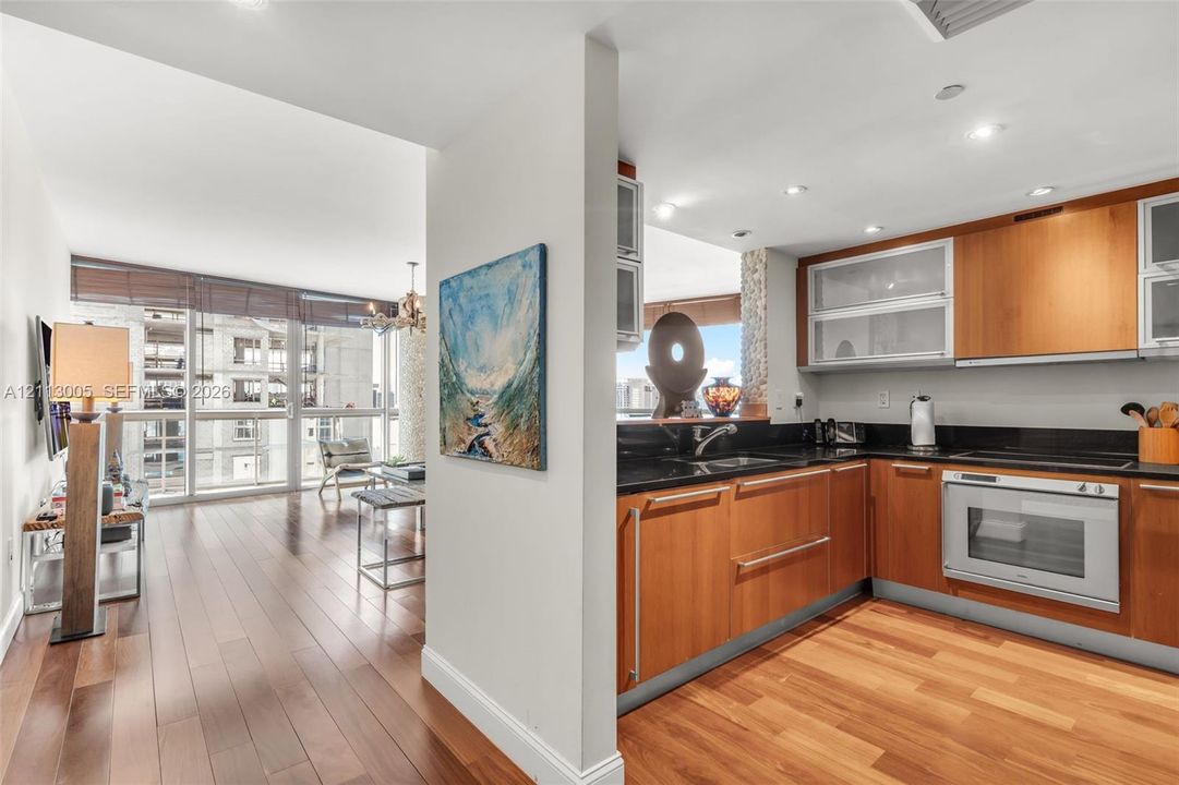 Kitchen featuring wood-finish cabinetry, dark stone-surface countertops, built-in oven, and recessed lighting, complemented by wood-finish flooring throughout