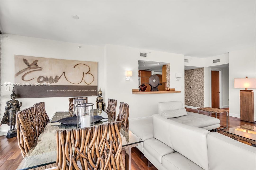 Open-concept living space featuring wood-finish flooring, a pass-through kitchen window with a built-in wooden ledge, wall-mounted light fixtures, and a decorative textured accent wall