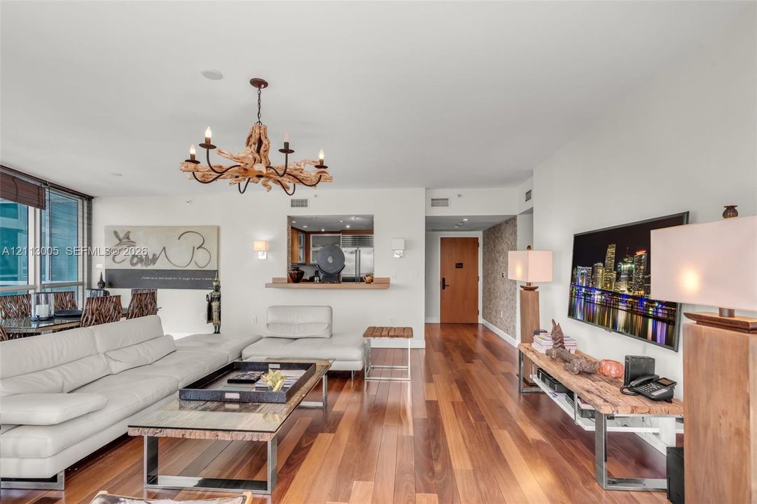 Open-concept living area featuring wood-finish flooring, a natural driftwood chandelier, textured wall accents, and a service pass-through window with a wood ledge