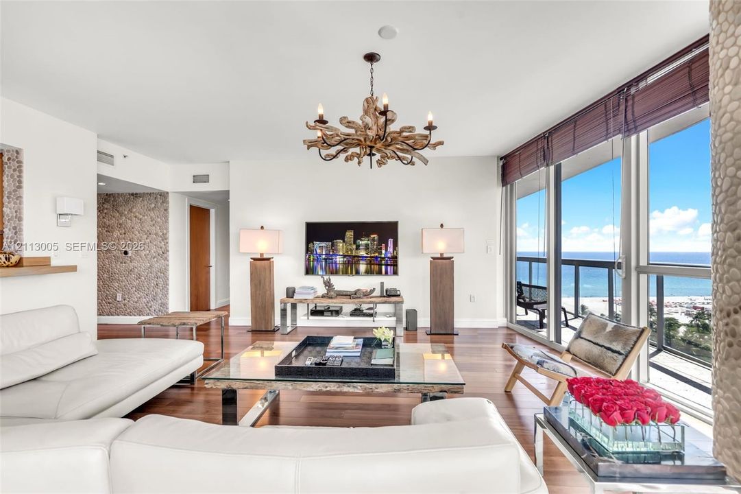 Living area featuring floor-to-ceiling windows, wood-finish flooring, decorative stone-textured wall accents, and an intricate statement chandelier