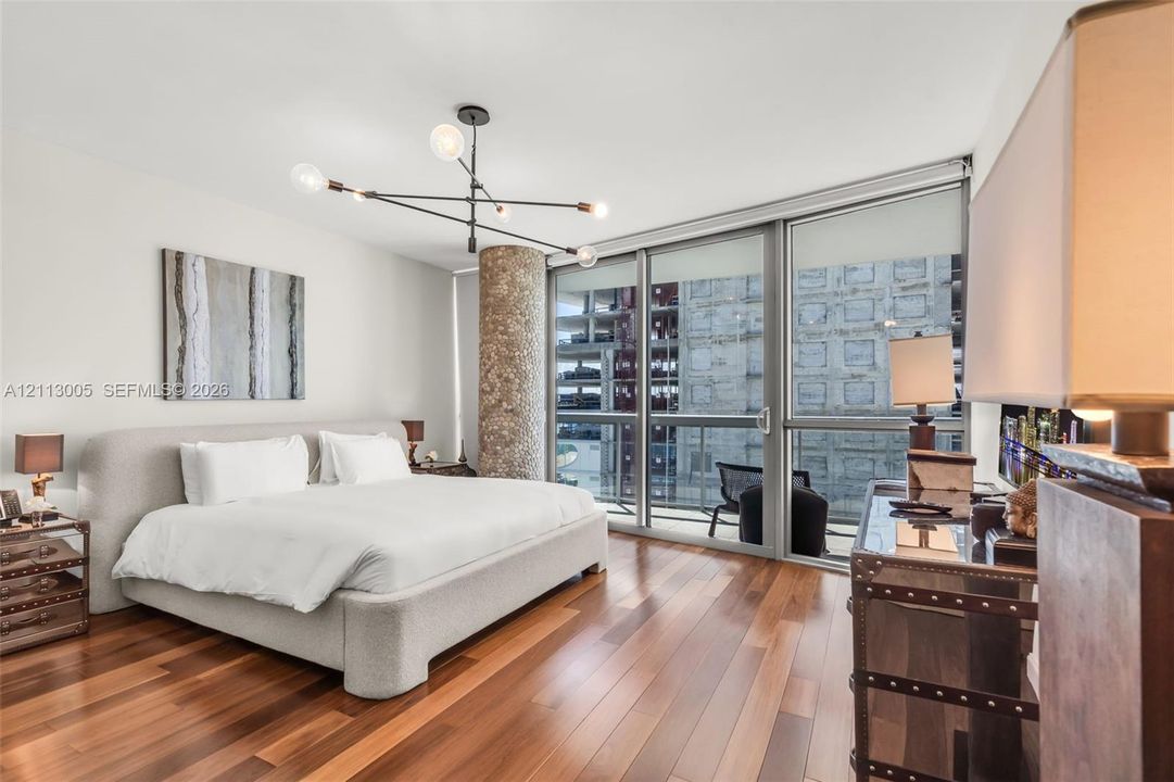 Floor-to-ceiling windows, wood-finish flooring, exposed textured structural column, multi-arm geometric light fixture, and glass sliding door access to exterior space