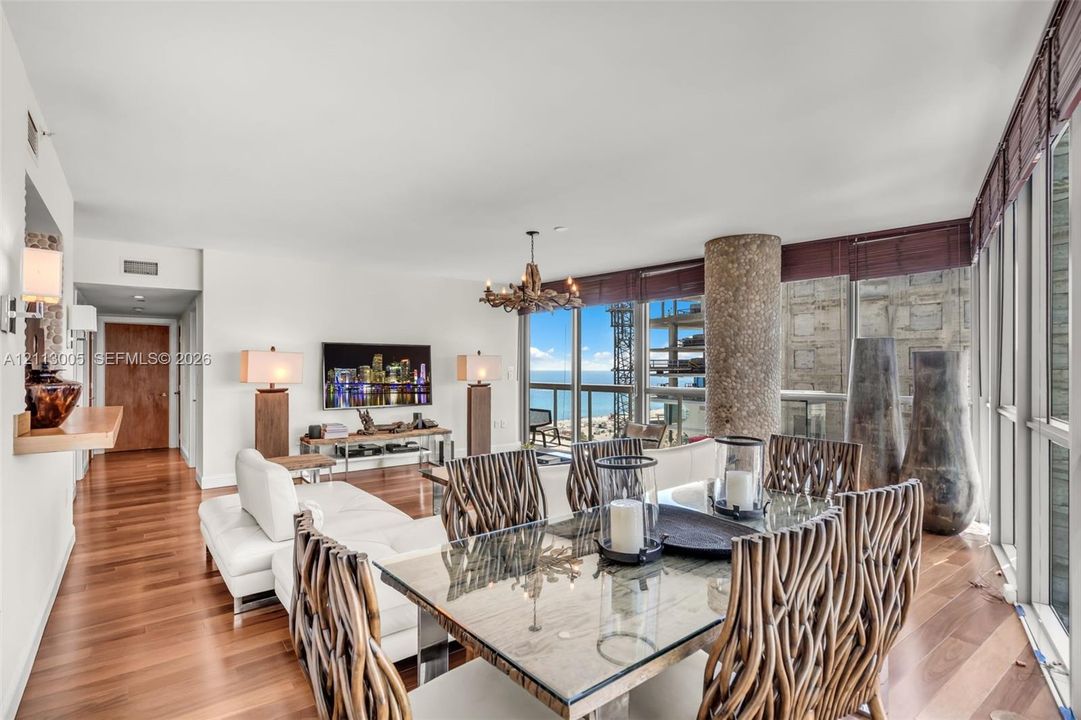 Open-concept interior featuring floor-to-ceiling windows, wood-finish flooring, a textured stone-clad support column, and custom chandelier lighting