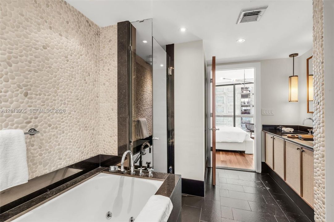 Bathroom featuring a deep soaking jetted tub, pebble-textured wall tiling, dark stone vanity countertop, slate tile flooring, and integrated pendant lighting