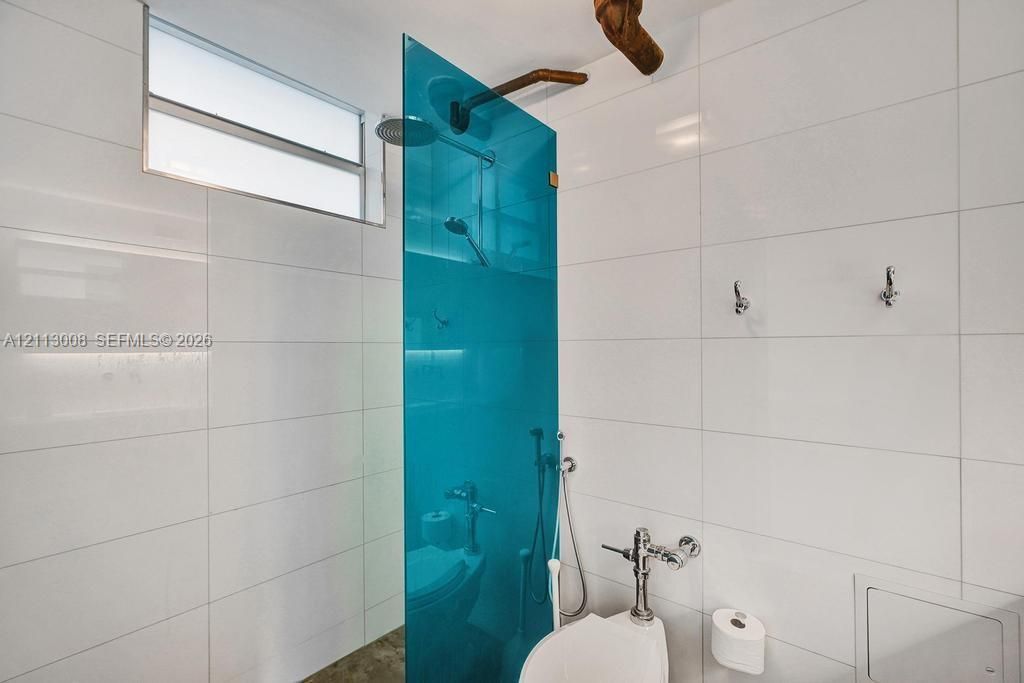 Shower featuring large-format white wall tile, a bold blue glass privacy screen, chrome rain shower head, and an exposed metallic pipe fixture