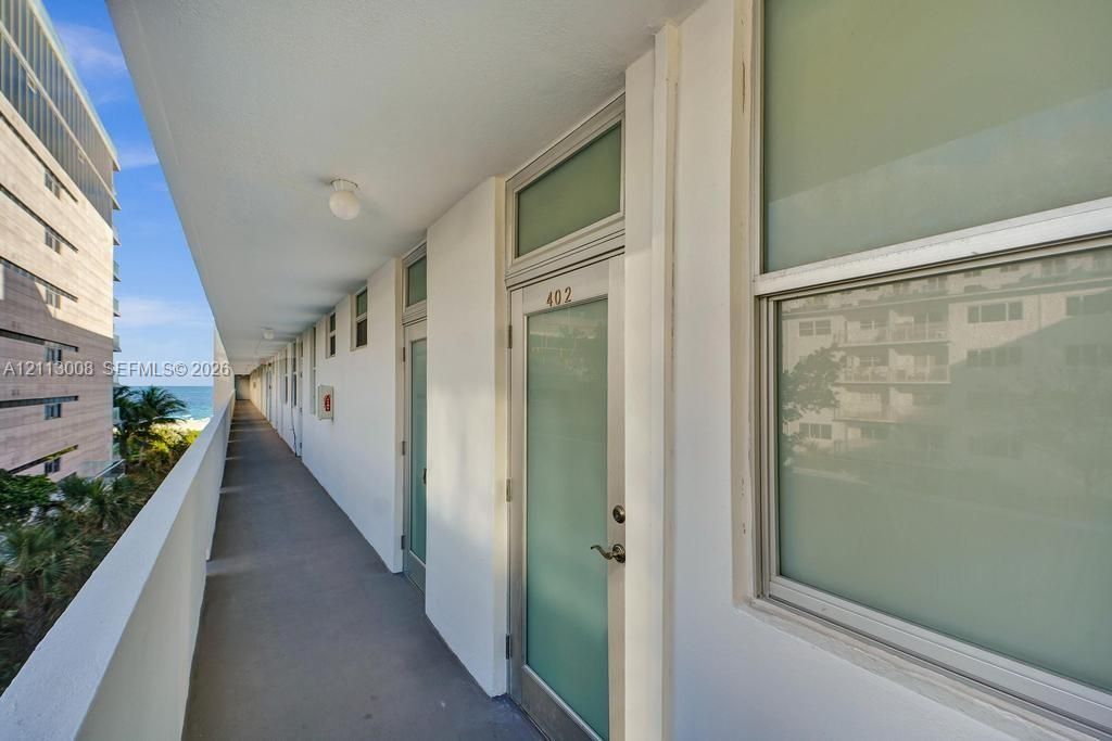 Covered exterior walkway featuring flush-mount lighting, glass-paneled entry doors with transom windows, and solid perimeter railings
