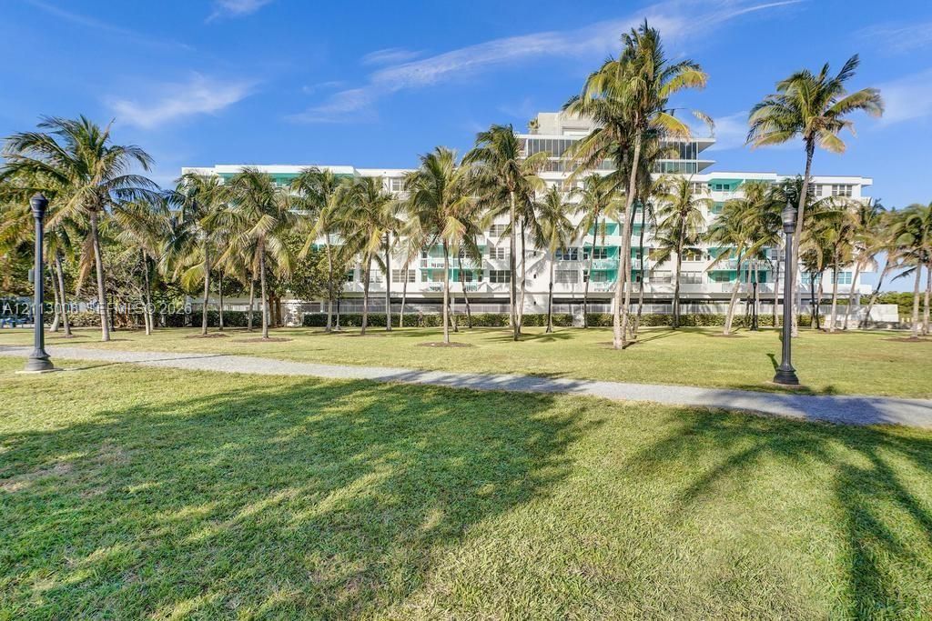 Multi-story residential building featuring exterior balconies, manicured lawn, paved pathways, and mature palm trees