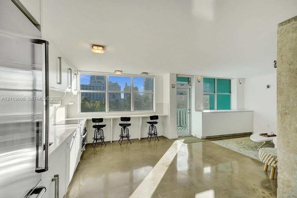 Kitchen featuring a polished concrete floor, white cabinetry, integrated stainless steel refrigerator, white countertops, and a built-in counter-height workspace