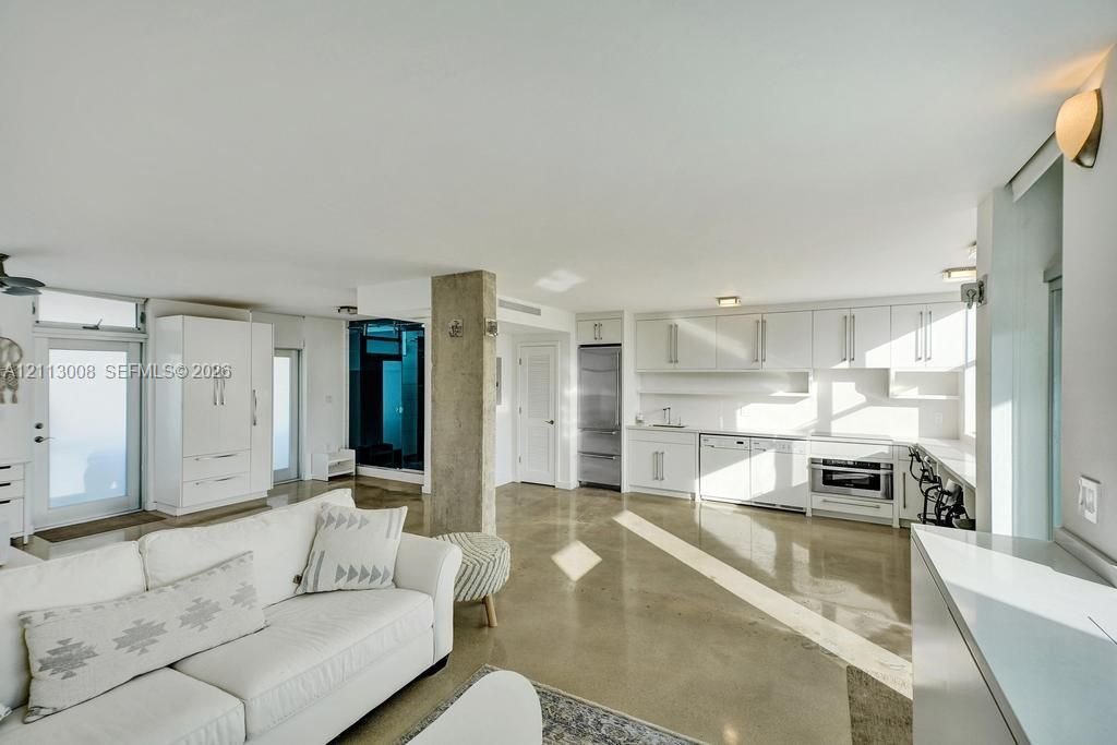 Open-concept interior featuring polished concrete flooring, white cabinetry, stainless steel appliances, and a central structural concrete pillar