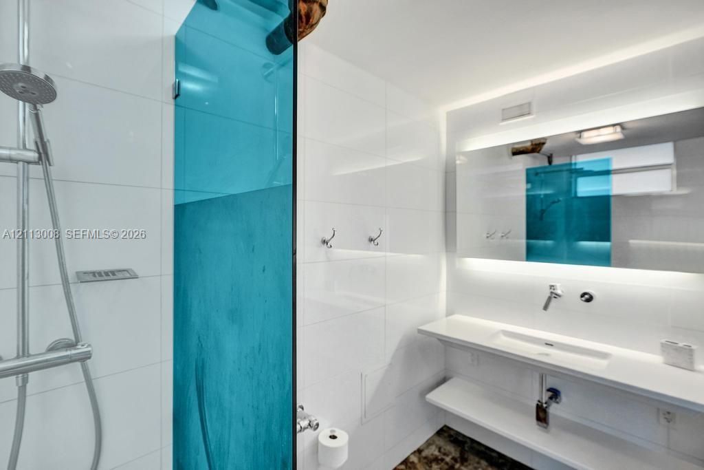 Modern bathroom featuring a wall-mounted floating vanity with an integrated sink, polished chrome faucet, expansive backlit mirror, and a glass-enclosed walk-in shower with large-format white tile wall cladding