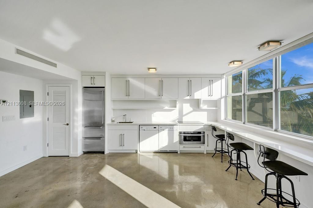 Kitchen featuring white cabinetry, stainless steel appliances, polished concrete flooring, a long built-in window counter, and expansive windows