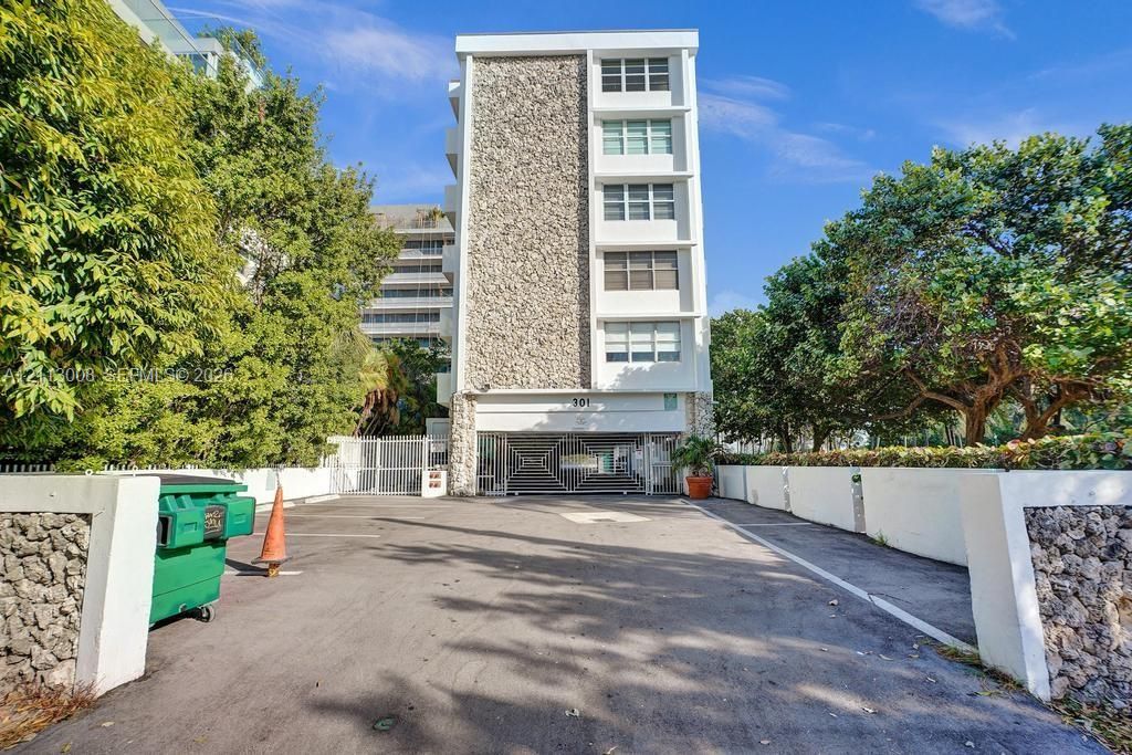 Multi-story building exterior featuring a textured stone facade, white stucco finish, asphalt parking area, and decorative metal security gate
