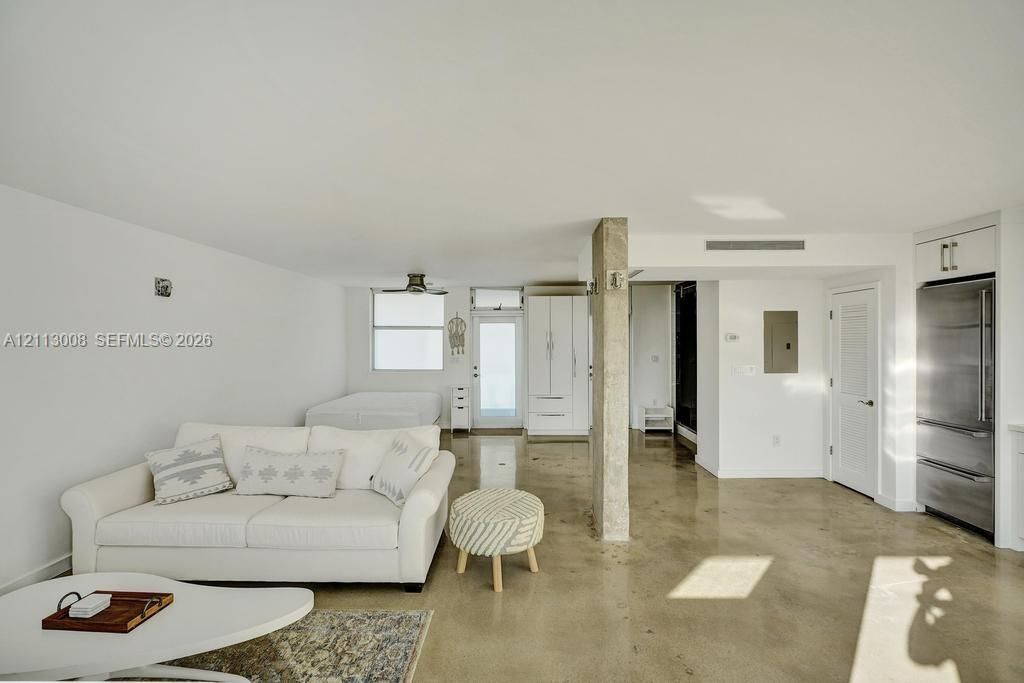 Polished concrete flooring, exposed concrete structural column, stainless steel refrigerator, and custom white cabinetry