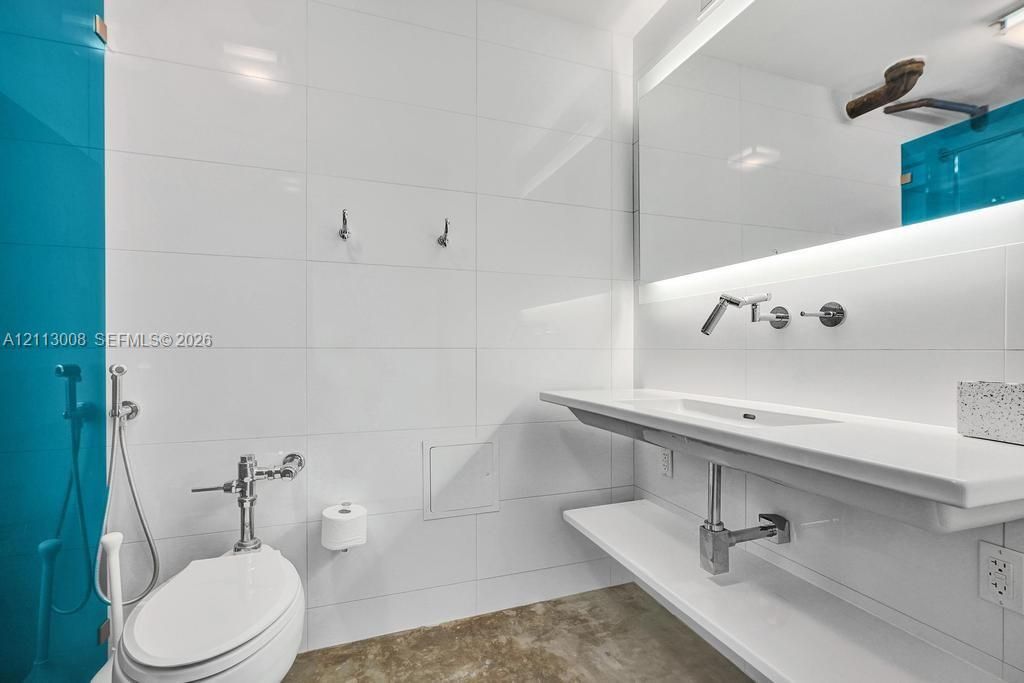 Modern bathroom featuring a wall-mounted floating vanity with an integrated sink, polished chrome wall-mounted faucet, large frameless mirror with perimeter lighting, and floor-to-ceiling tiled walls with blue accent tiling