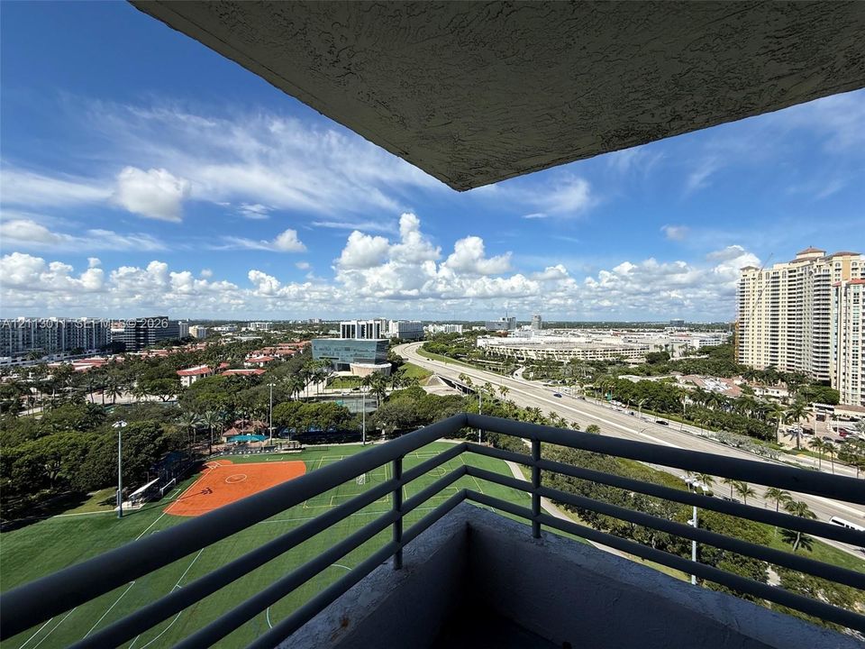 Private balcony featuring metal railings and a panoramic perspective of the surrounding cityscape and local recreational grounds