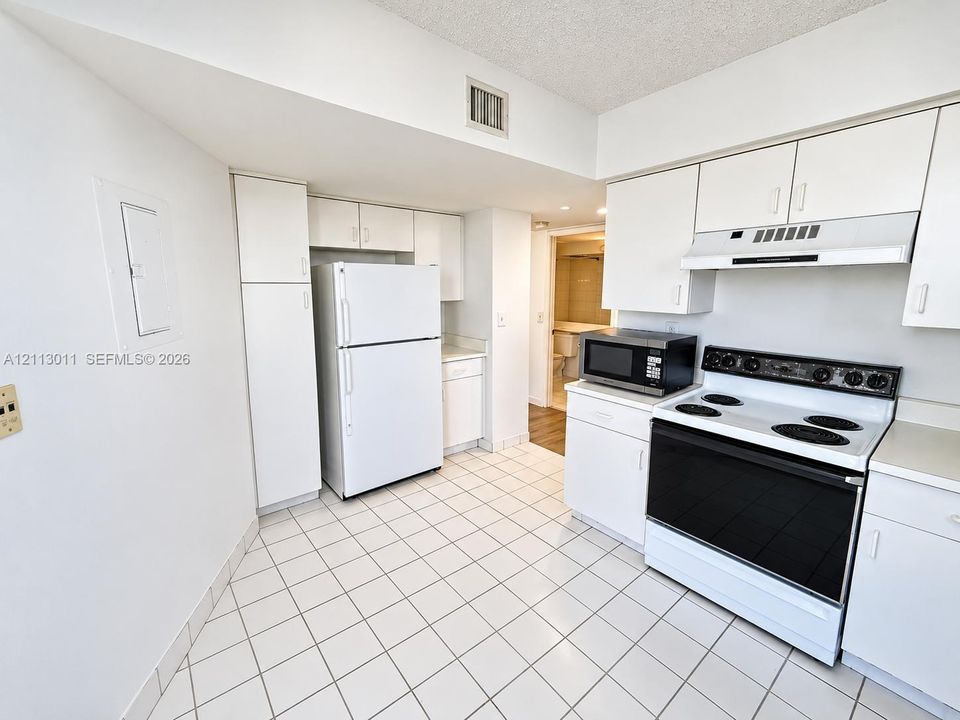 Kitchen featuring white cabinetry, ceramic tile flooring, a solid-surface range with a hood, and a full-size refrigerator