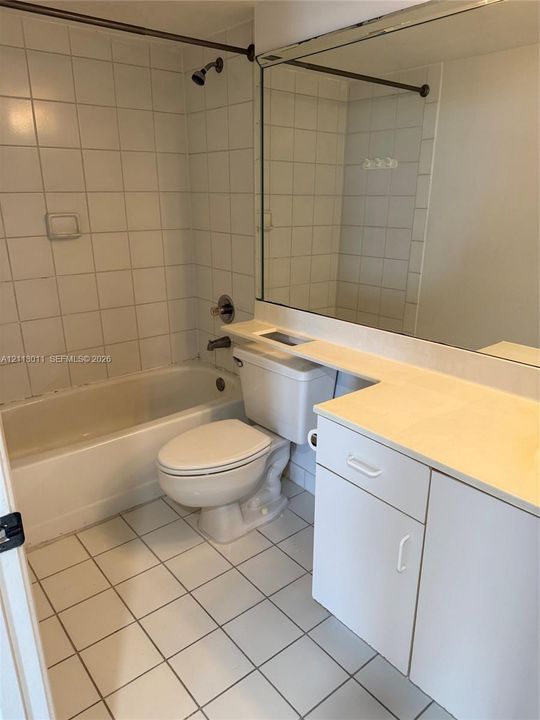 Bathroom featuring a white vanity cabinet with an integrated countertop, square tile flooring, a shower-tub combination with wall-mounted plumbing fixtures, and a wall-to-wall mirror