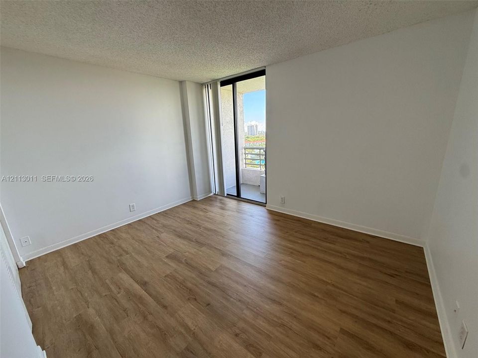 Room featuring wood-finish flooring, a neutral color palette, and a floor-to-ceiling glass sliding door providing access to a private balcony