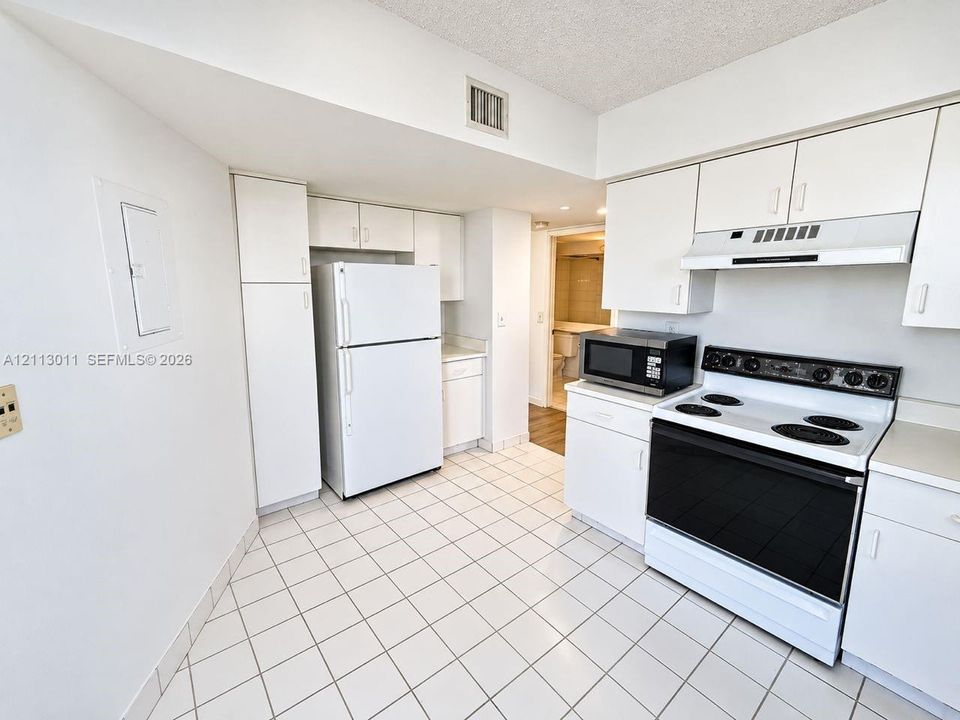 Kitchen featuring white cabinetry, solid-surface countertops, tile flooring, and integrated white appliances
