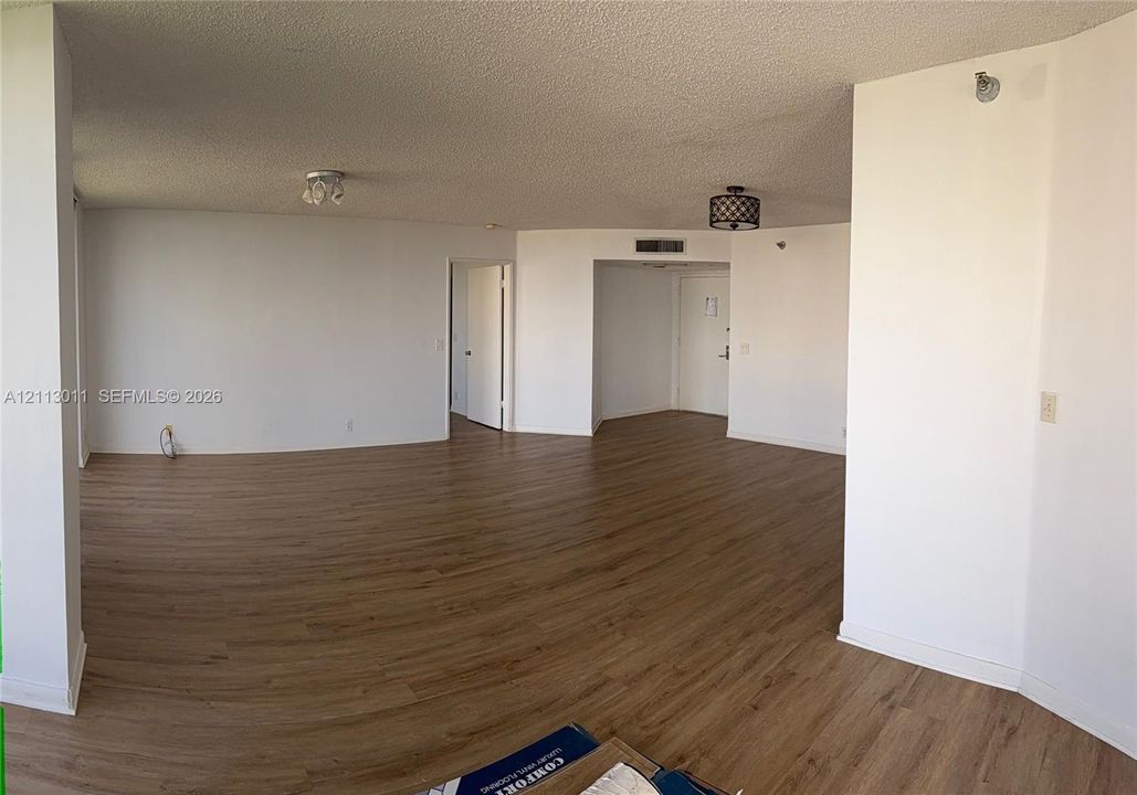 Open-concept interior featuring wood-finish flooring, textured ceilings, and dual drum-style ceiling light fixtures