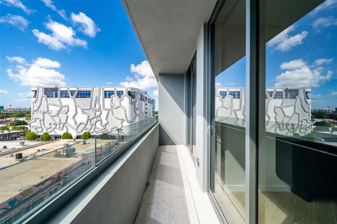 Covered balcony featuring concrete flooring, a glass panel railing, and full-height sliding glass doors