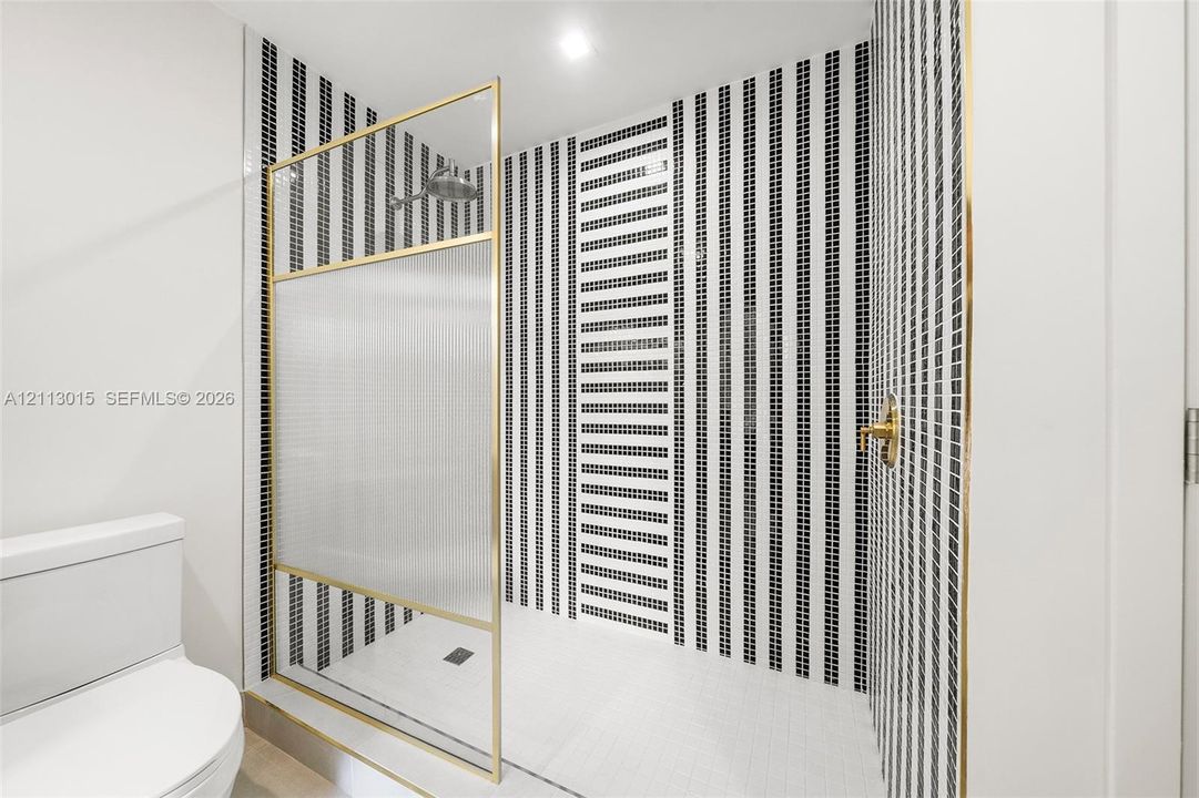 Walk-in shower featuring a brass-framed glass enclosure, floor-to-ceiling vertically striped mosaic tile work, and gold-finish plumbing fixtures