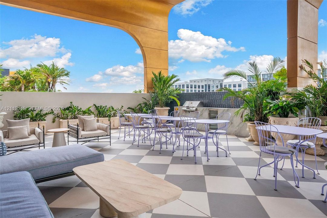 Covered terrace featuring geometric tile flooring, built-in outdoor kitchen with stone-finish cabinetry, and solid archway support