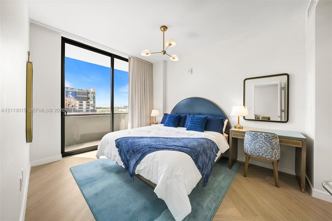 Herringbone-patterned wood-finish flooring, floor-to-ceiling sliding glass doors, private balcony, and contemporary multi-arm chandelier