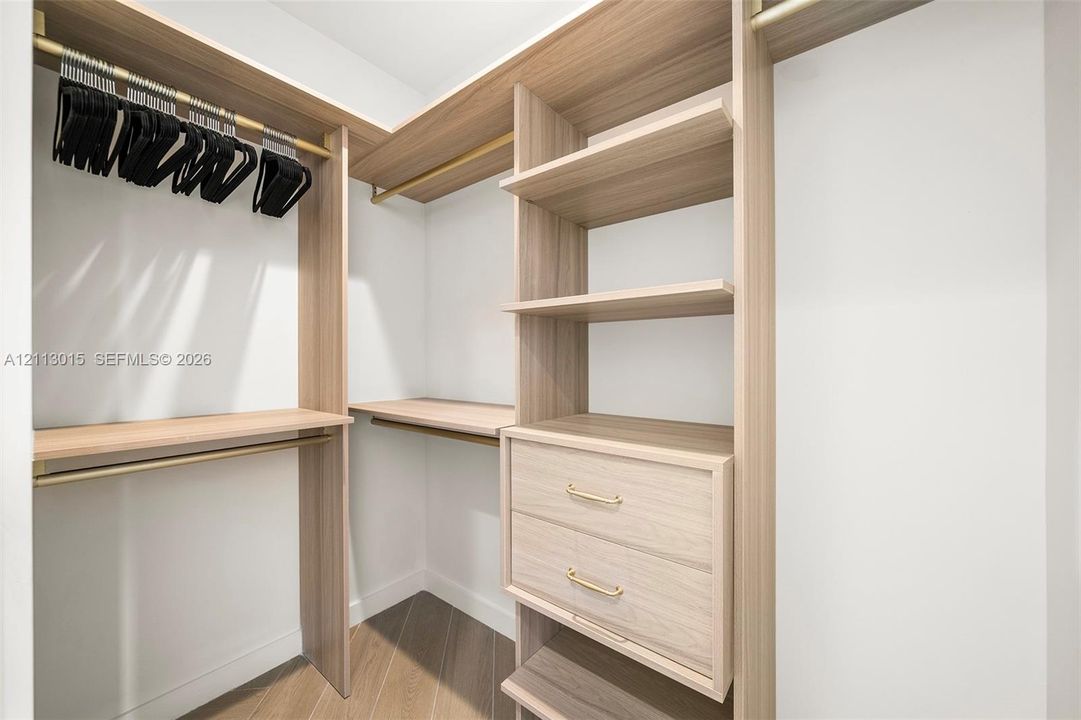 Custom reach-in closet featuring wood-finish cabinetry, built-in shelving, double drawers with gold-tone hardware, and integrated brass-finish garment rods
