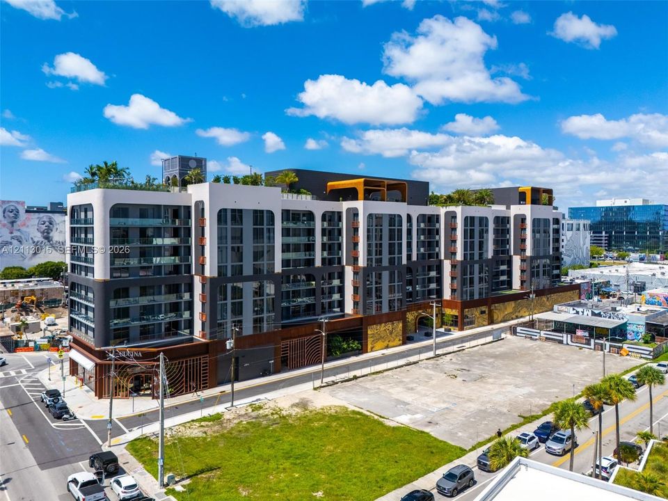 Multi-story architectural complex featuring a contemporary facade with integrated balconies, metallic exterior accents, ground-level retail frontage, and rooftop terrace space