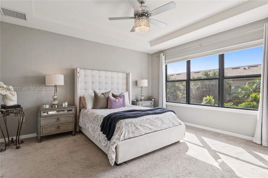 Tray ceiling, large multi-pane window, and decorative ceiling fan with integrated crystal-style lighting