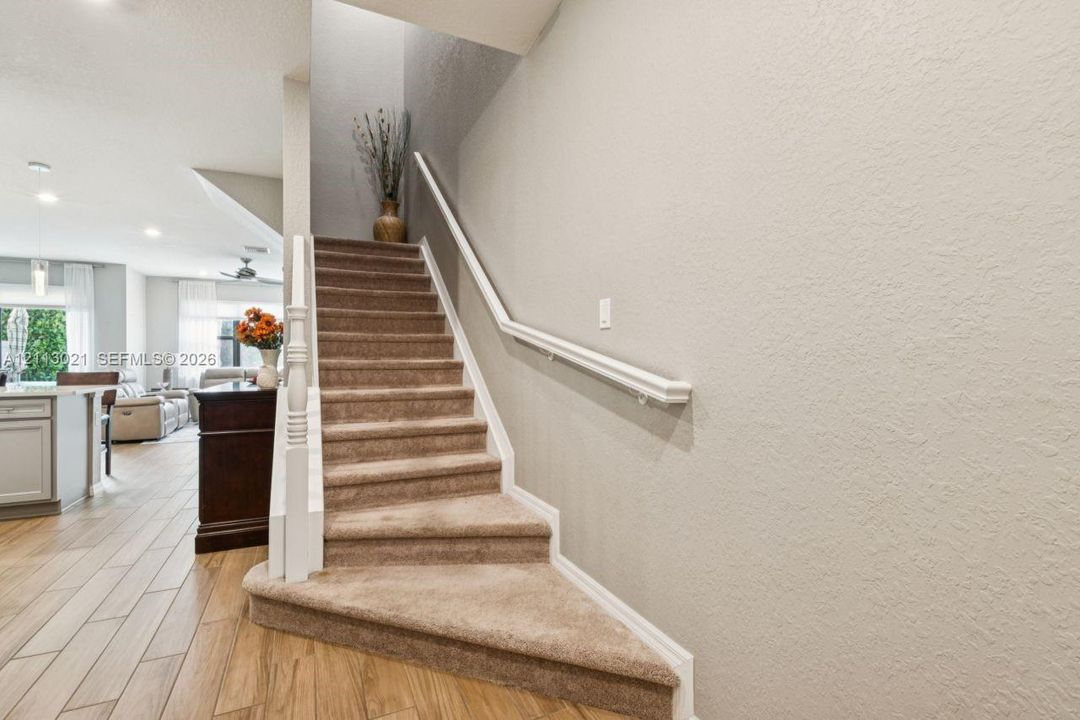 Staircase featuring carpeted treads, a white wood baluster, and a wall-mounted handrail, set against wood-finish flooring