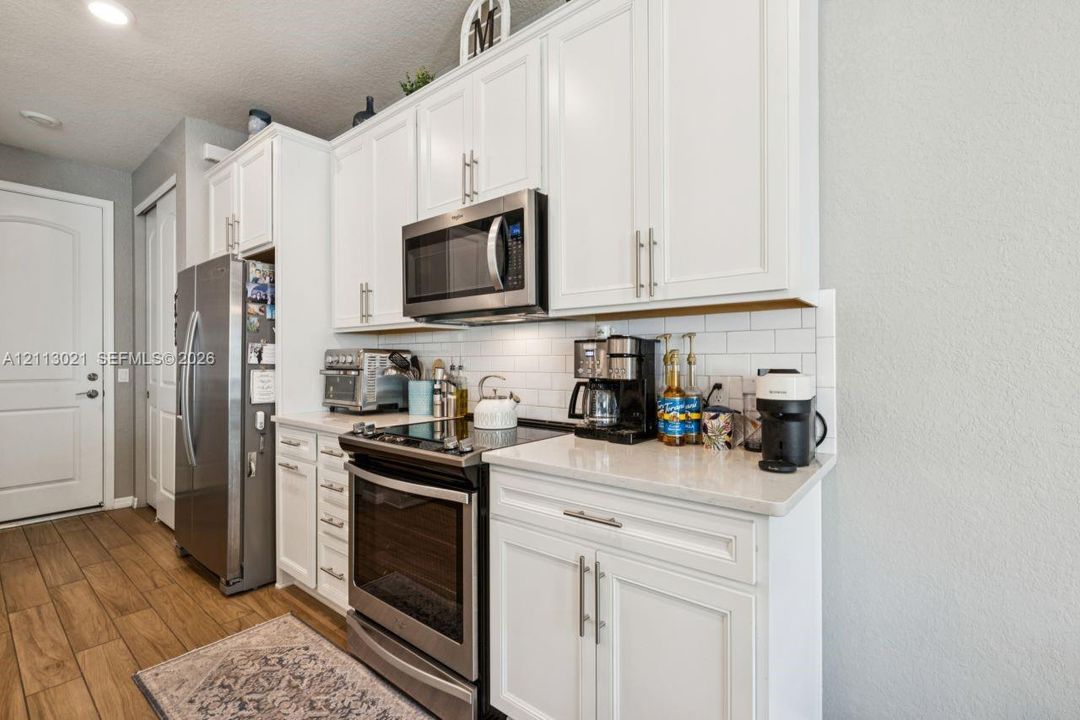 Kitchen featuring white Shaker-style cabinetry, stainless steel appliances, quartz countertops, and a white subway tile backsplash, complemented by wood-finish flooring