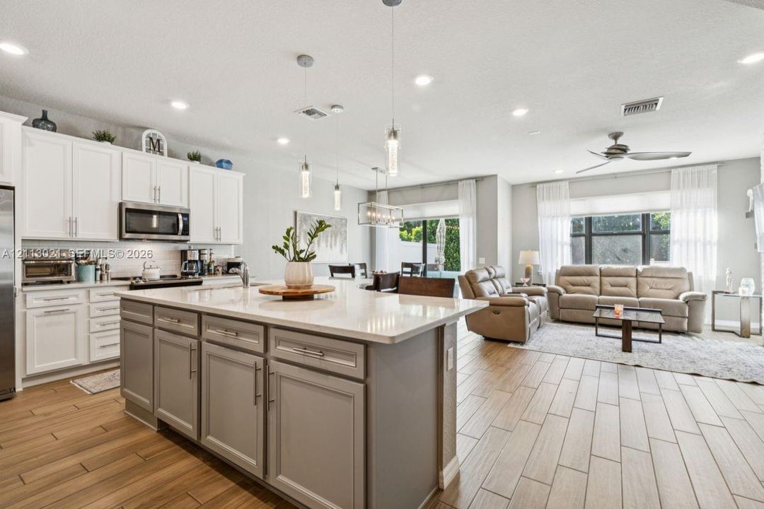 Kitchen featuring an expansive center island with stone-finish countertops, ceiling-mounted pendant lighting, shaker-style cabinetry, and wood-finish flooring
